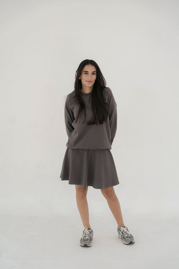 Woman wearing a grey skirt with matching top with a plain background