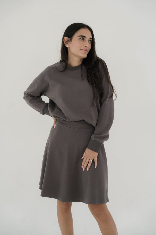 Woman wearing a gray sweater and skirt set against a plain background